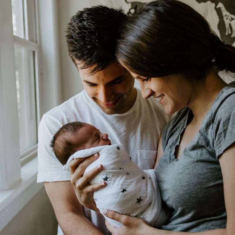 woman holding baby beside man smiling